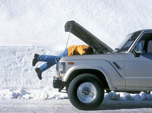 Man repairing 4x4 automobile in snow, side view